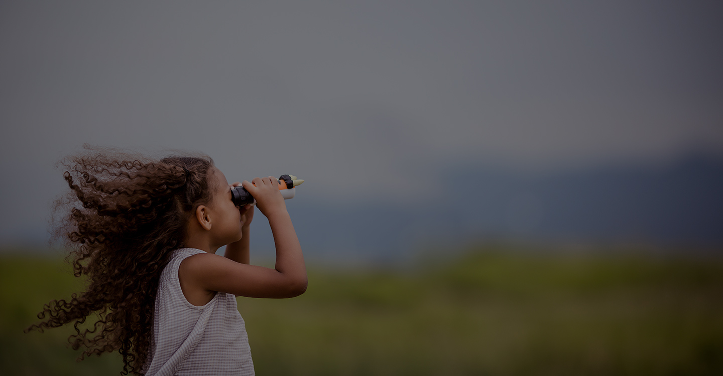 Young girl in a field looking through binoculars 